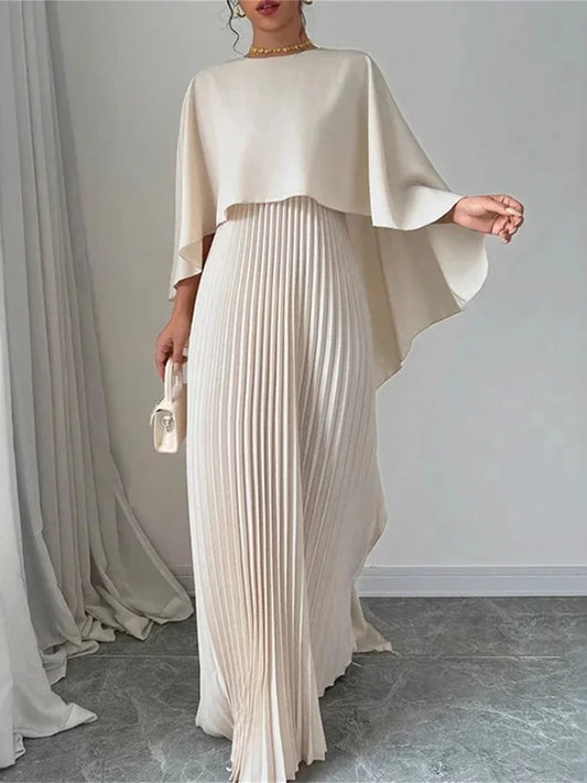 Woman wearing an ivory cape overlay pleated maxi dress in a minimalist setting.
