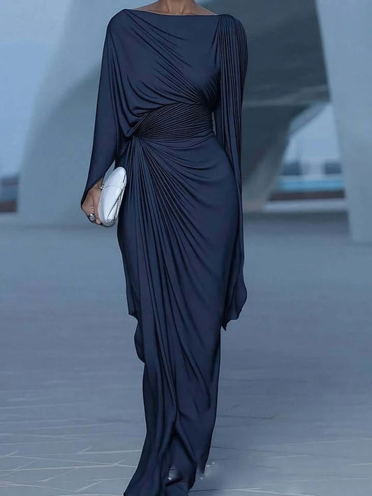 Elegant woman wearing a midnight blue draped evening dress with asymmetric gathers in a modern architectural setting.