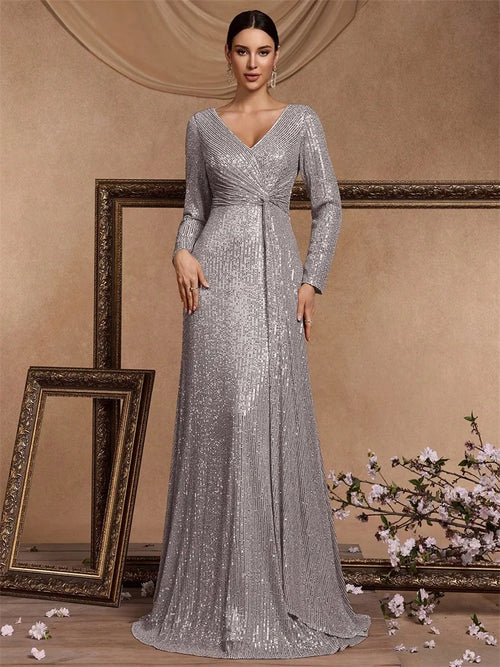 Elegant woman wearing a silver sequined long-sleeve evening gown with a draped waist in a classic studio setting.
