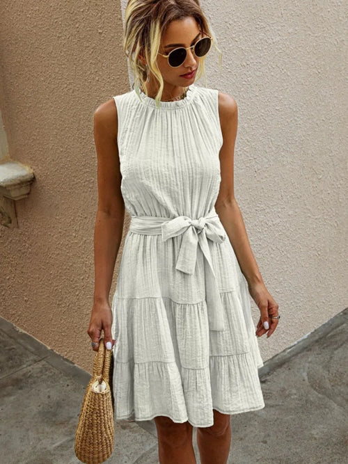 Model wearing a white sleeveless mini dress with waist tie and tiered skirt, casual and elegant summer outfit.